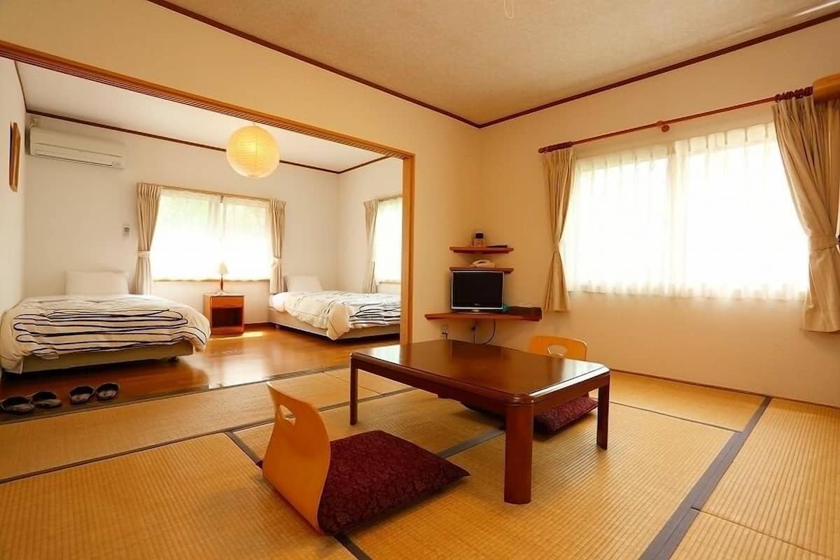 Ein traditioneller japanischer Raum mit Tatami-Boden, Futon-Bett, niedrigem Tisch und Fernseher.