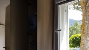 A bedroom with a bed, a wardrobe, and a window with a view of greenery and mountains.