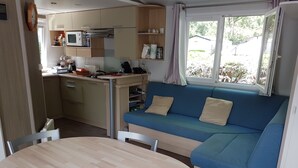 A compact kitchenette with a microwave, stove, and sink. There is a blue sofa with cushions and a dining table with chairs.