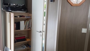 A room with a television on a stand, a bookshelf, a door, and a window with a view.