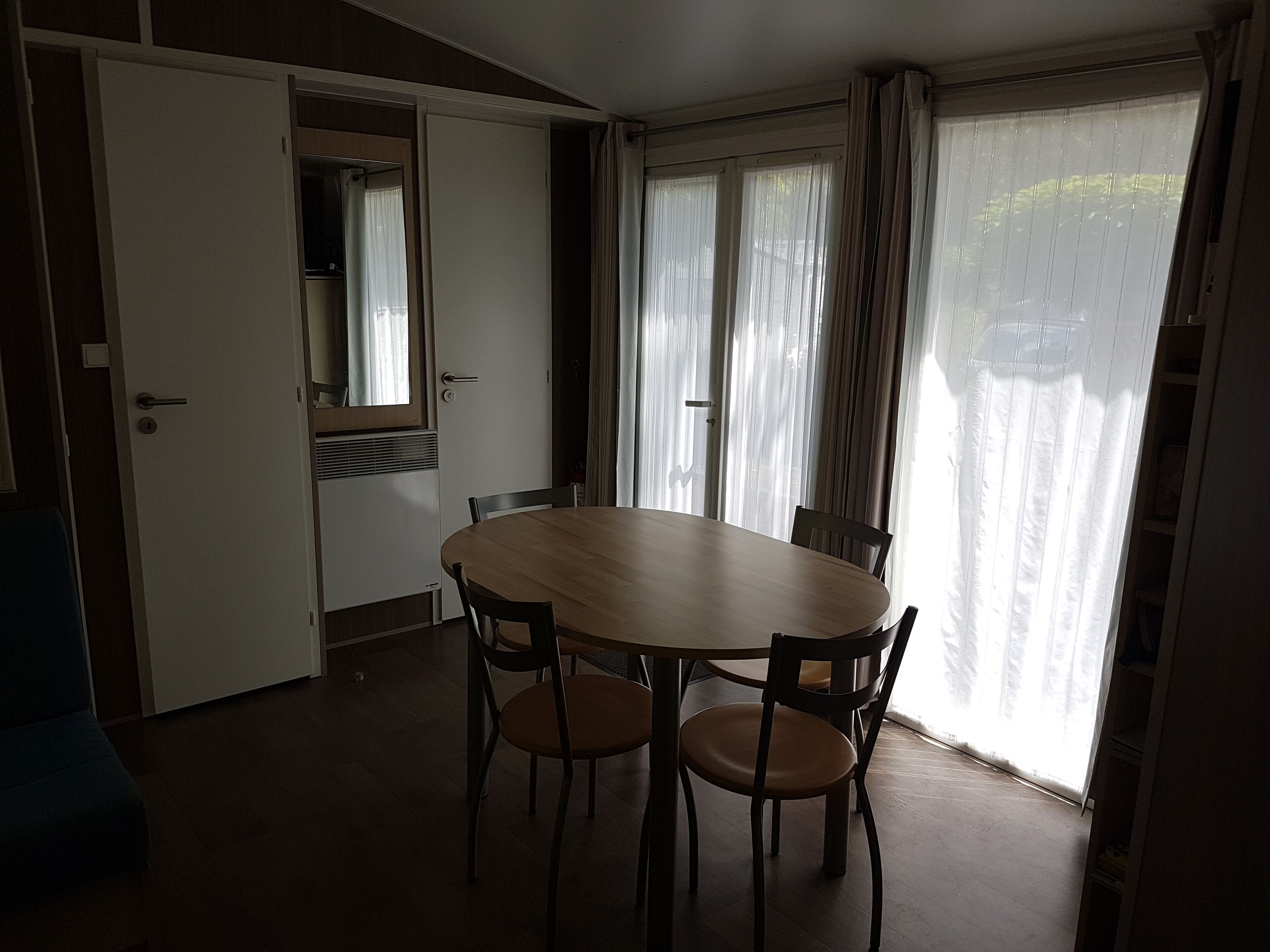 Uma área de refeições com uma mesa redonda e quatro cadeiras, uma porta deslizante e uma janela com cortinas.