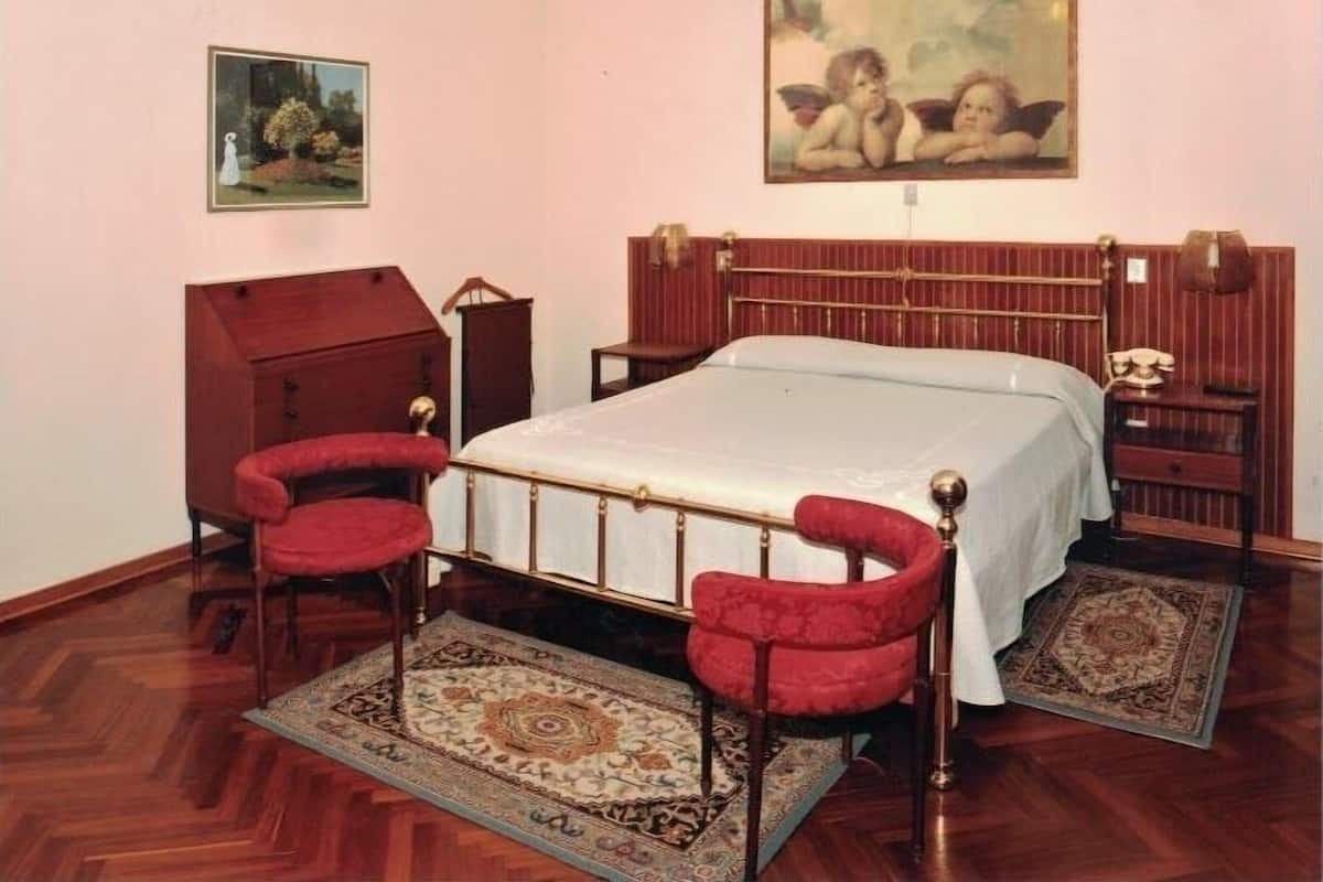 A bedroom with a wooden bed frame, a red upholstered chair, a nightstand, and a painting on the wall.