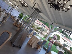 An outdoor dining area with tables and chairs, a central column, and a view of a garden and buildings in the background. - Albergo La Perla Della Valle (Civitella Roveto)