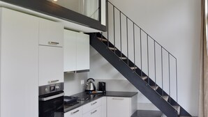 A modern kitchen with white cabinets, a black countertop, and a stainless steel oven. There is a staircase with a black railing leading to an upper level. - The Loft Interlaken (Interlaken)