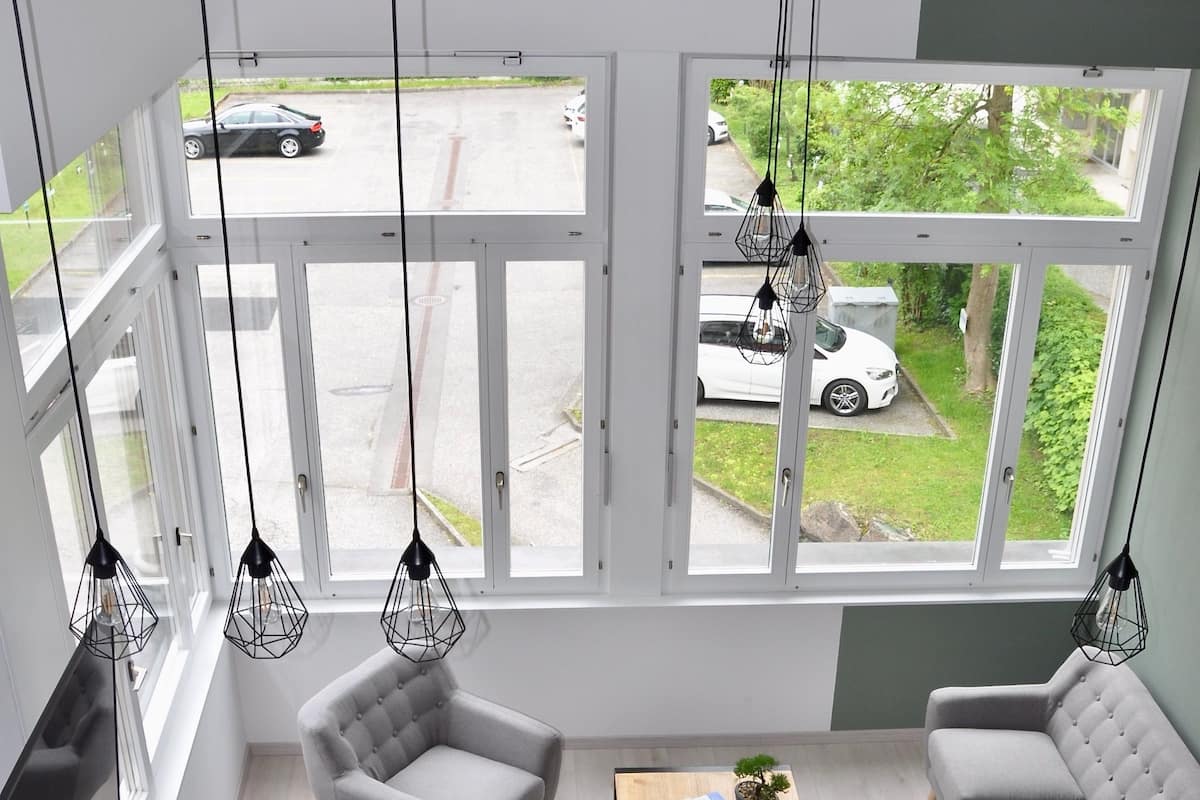 A modern living room with a dining area, large windows, and hanging light fixtures.