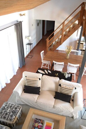 Ein großzügiger Wohnbereich mit weißem Sofa, einem Esstisch mit Stühlen, einer Treppe und Blick ins Freie.