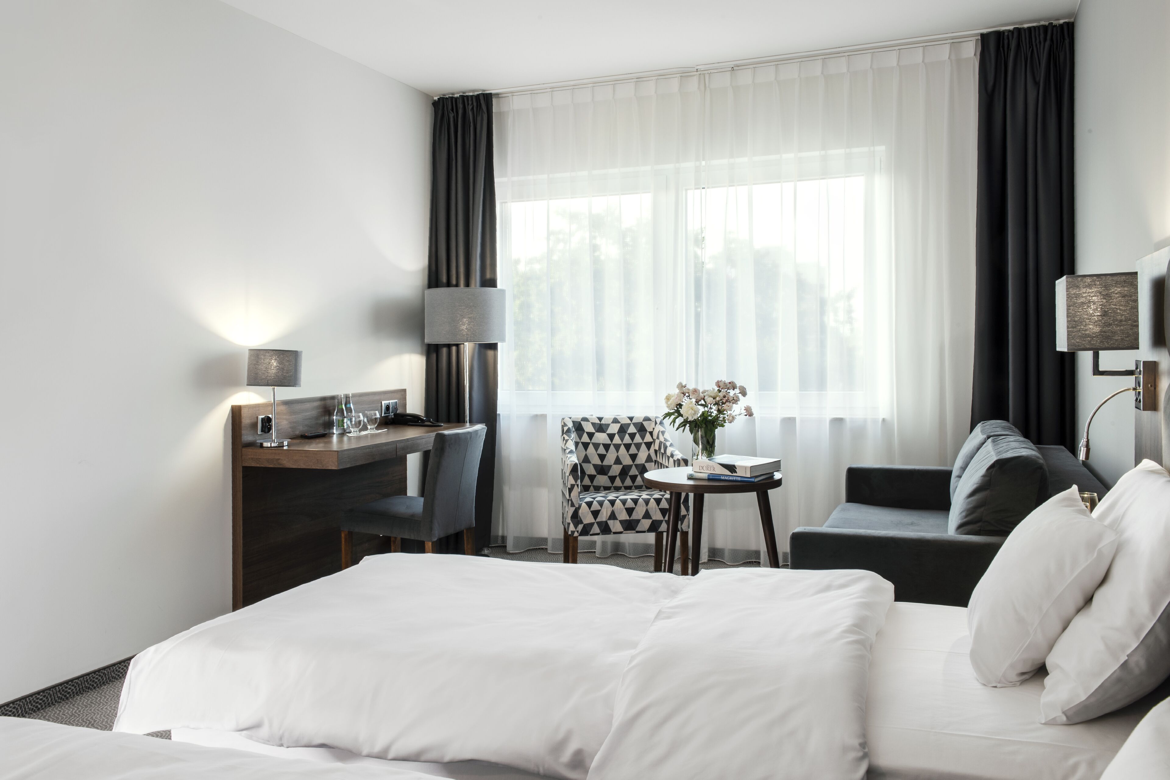 A hotel room with a bed, a desk, a chair, and a sofa.