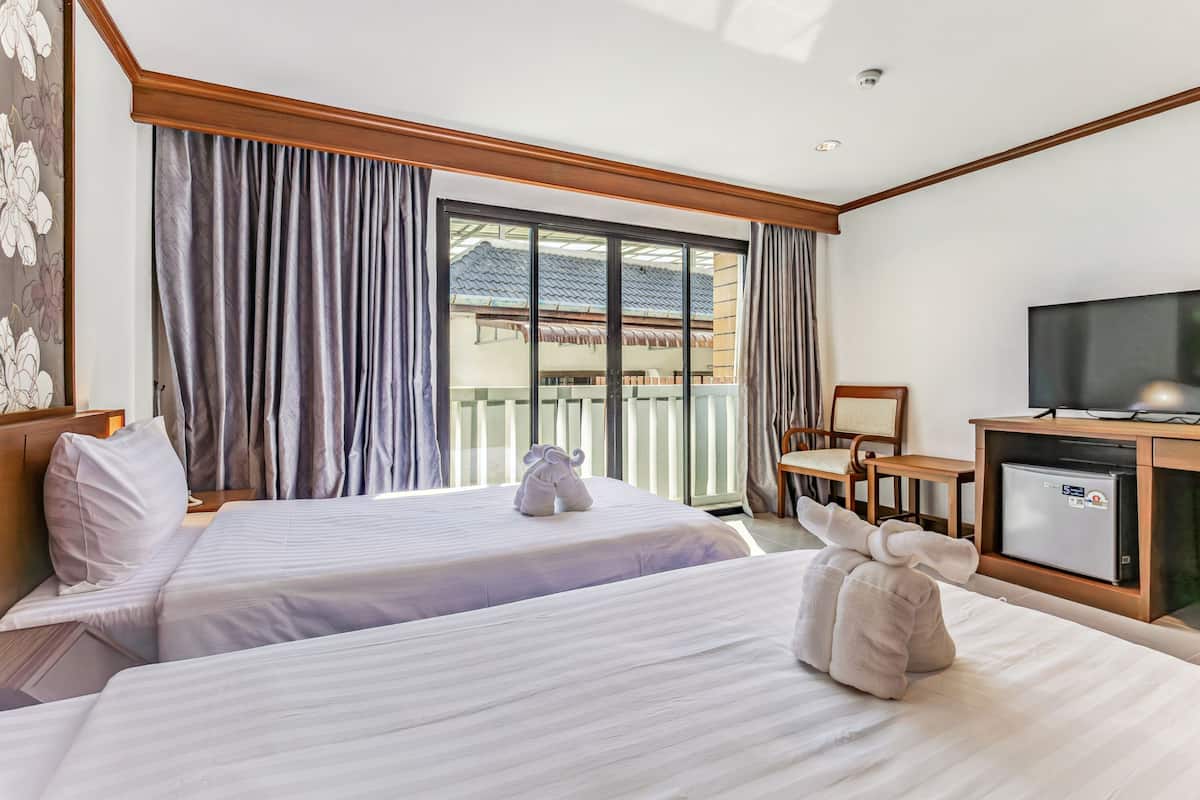 A hotel room with two beds, a television, a small desk, and a balcony with curtains.