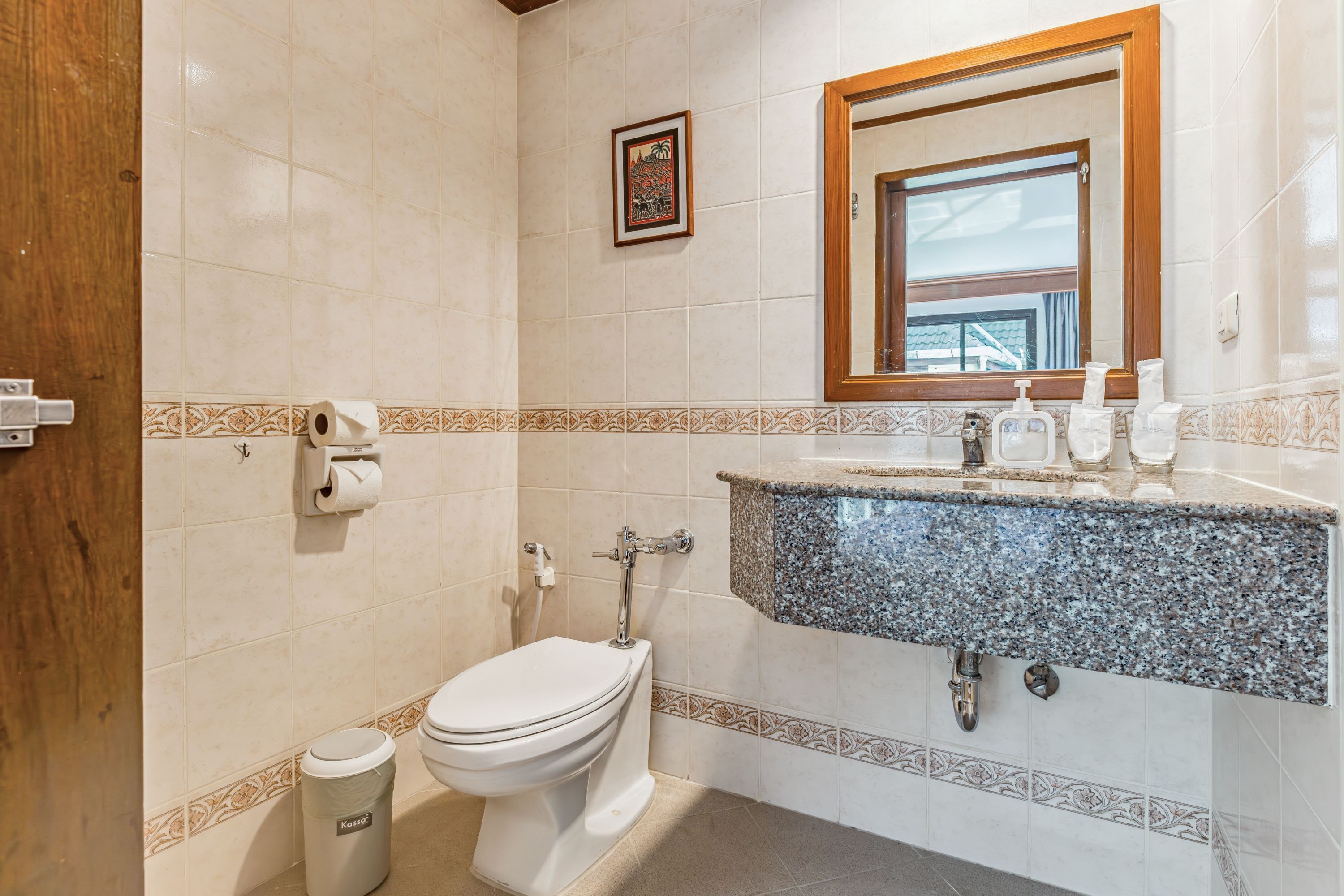 Un baño con inodoro, lavamanos y una ventana enmarcada sobre el espejo.
