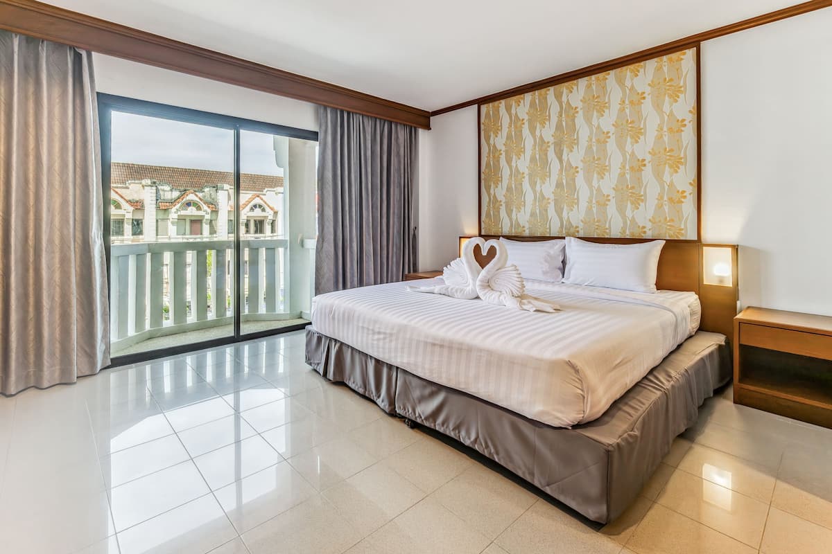 A hotel room with a large bed, a balcony with curtains, and a view of buildings outside.