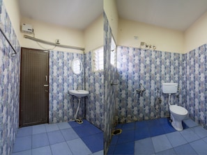 A bathroom with a toilet, sink, and shower. The walls are tiled with a blue and white pattern. - Lusia Inn (Bengaluru)