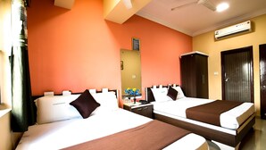 A hotel room with two beds, a ceiling fan, an air conditioning unit, a nightstand with a phone and a vase of flowers, and a door with a mirror. - Lusia Inn (Bengaluru)