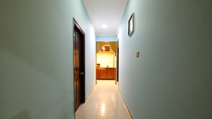 A hallway with light blue walls, a wooden door on the left, and a wooden counter in the distance. - Lusia Inn (Bengaluru)