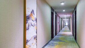 A long, narrow hotel corridor with a colorful carpet, a large abstract painting on the left wall, and a series of doors on the right. - Oriental Beauty Hotel (Guangzhou)