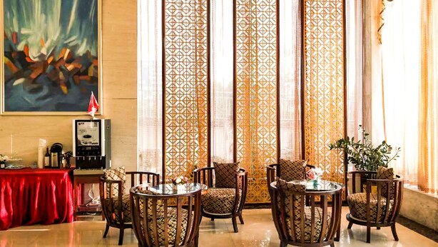 A hotel lobby with a red table, six wooden chairs with patterned cushions, a large abstract painting, and a decorative screen with geometric patterns. - Oriental Beauty Hotel (Guangzhou)
