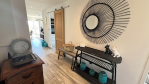 A hallway with a wooden bench, a black metal console table with teal vases, a wall clock, and a large black mirror. - LE VICTORIA SANARY CENTER TOP FLOOR SEA VIEW<br>SPACIOUS ELEGANT APARTMENT (Sanary-sur-Mer)