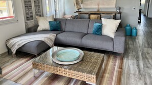 A living room with a grey sofa, a woven coffee table, and a large painting on the wall. - LE VICTORIA SANARY CENTER TOP FLOOR SEA VIEW<br>SPACIOUS ELEGANT APARTMENT (Sanary-sur-Mer)