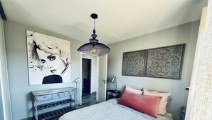 A bedroom with a bed, a dresser, a painting, a pendant light, and a decorative wall piece. - LE VICTORIA SANARY CENTER TOP FLOOR SEA VIEW<br>SPACIOUS ELEGANT APARTMENT (Sanary-sur-Mer)