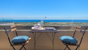 Un balcon avec deux chaises, une table, un chapeau, un verre de vin et un livre.