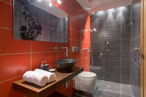 Un baño moderno con un espejo grande, un lavabo redondo, un inodoro y una cabina de ducha de vidrio.