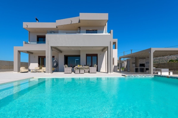 Una casa moderna de dos pisos con piscina, mobiliario exterior y una pérgola.