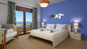 Une chambre dotée d’un grand lit, de deux tables de chevet, d’une chaise, d’un balcon avec des rideaux et d’une vue sur la mer.