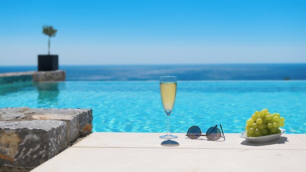 On peut clairement voir une piscine, avec une coupe de champagne et un bol de raisins sur une terrasse ensoleillée.