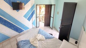 A bedroom with a bed, a wardrobe, a TV, and a door leading to a balcony. - Pousada D'Ibiza (Itanhaém)
