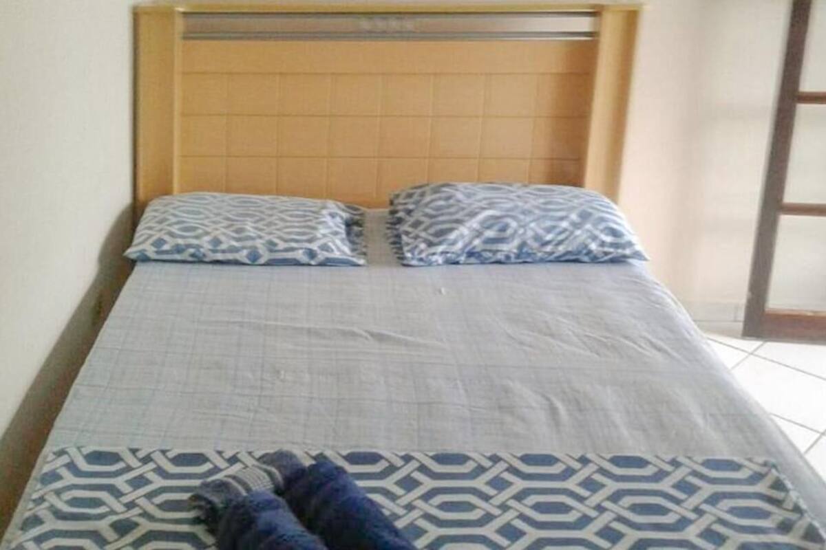 A bed with a patterned bedspread and pillows, a wooden headboard, and a view of a tiled floor and a door.