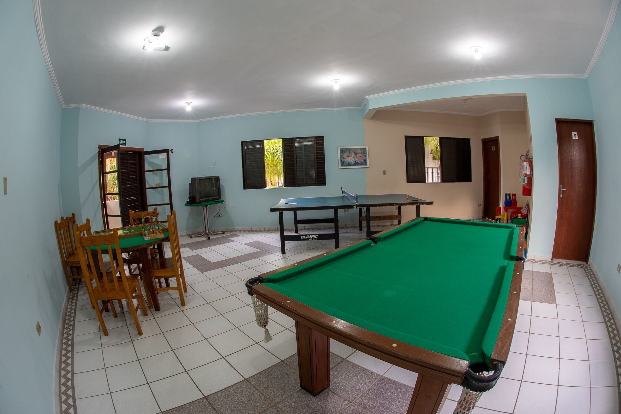 A room with a pool table, a dining table with chairs, and a television.