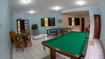 A room with a pool table, a dining table with chairs, and a television.