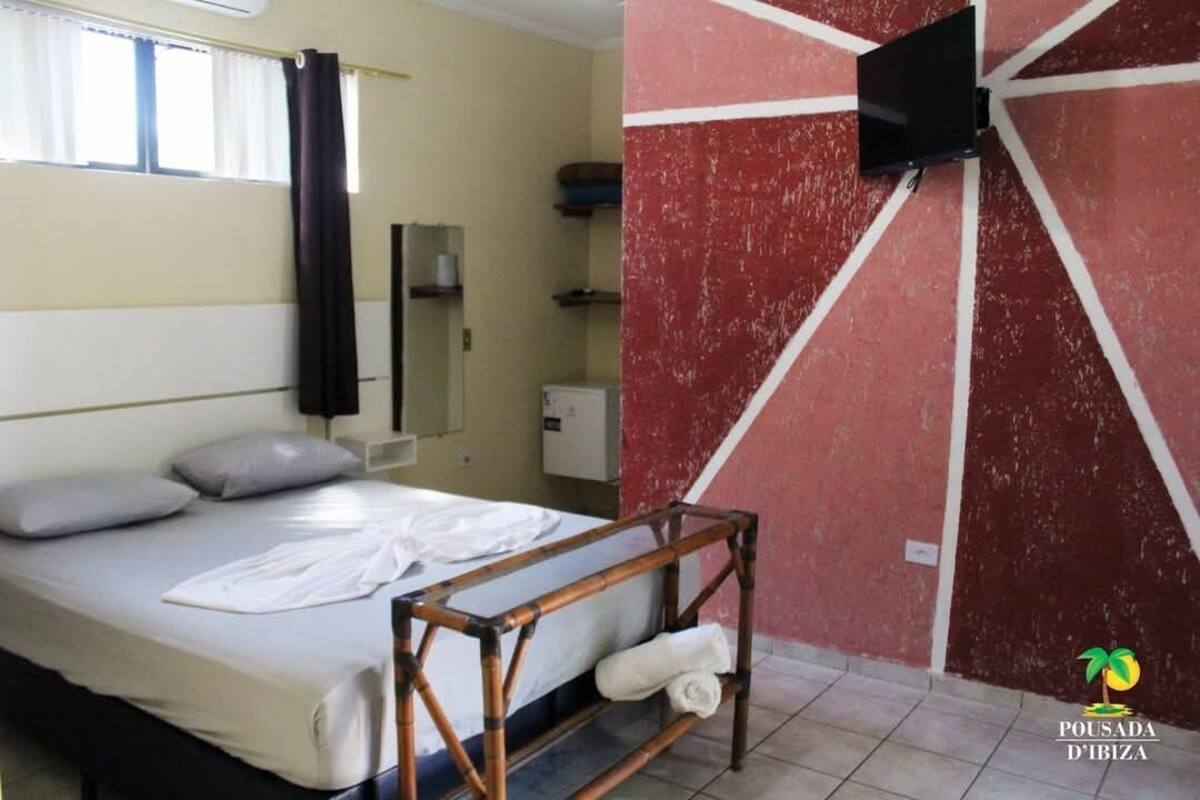 A hotel room with a bed, a TV mounted on the wall, and a red and white wall design.
