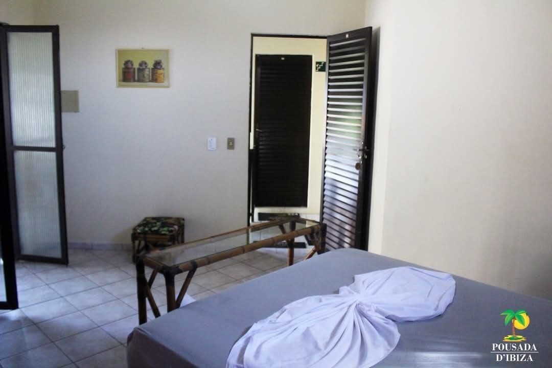 Una habitación de hotel con una cama, una mesita, un banco y una puerta.