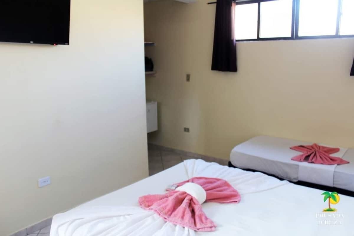 A room with two beds, each with a towel. There is a television on the wall and a window with curtains.