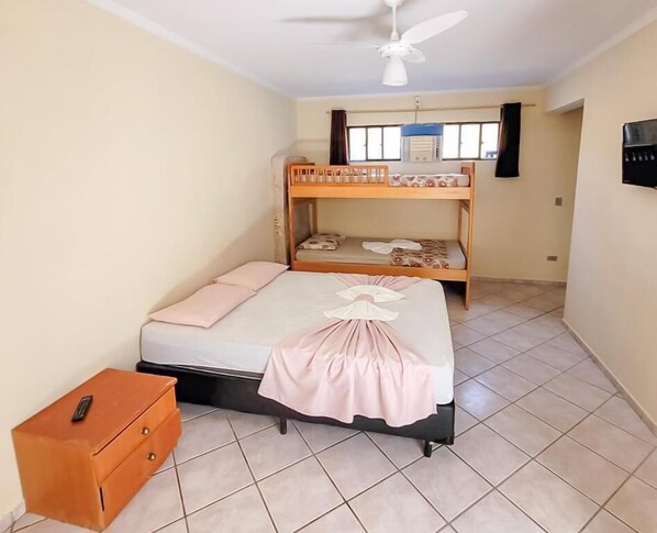 A bedroom with a bunk bed, a single bed, a ceiling fan, a heater, and a small wooden cabinet.