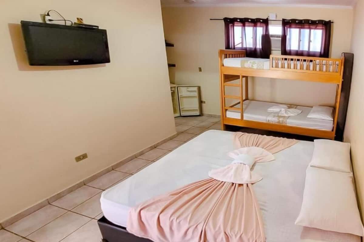 A hotel room with a bunk bed, a flat-screen TV mounted on the wall, and a neatly made bed with a towel.