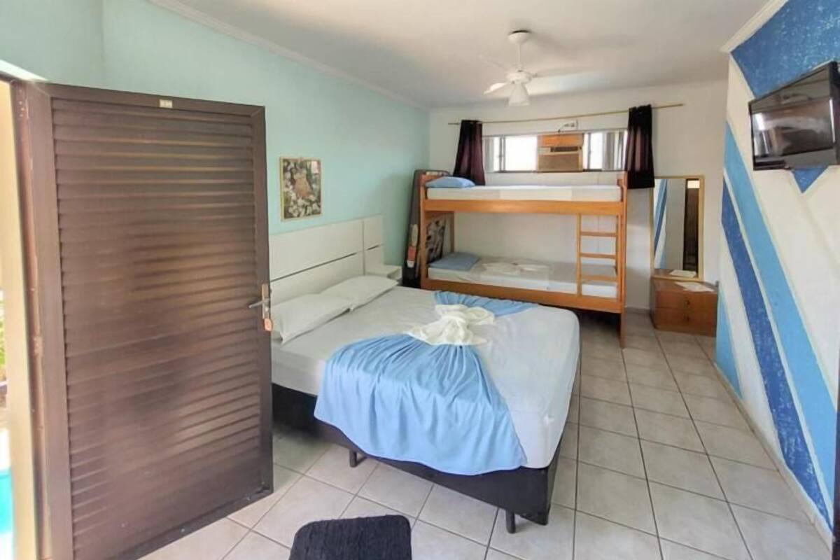 A room with a bed, a bunk bed, a ceiling fan, a TV, and a door.