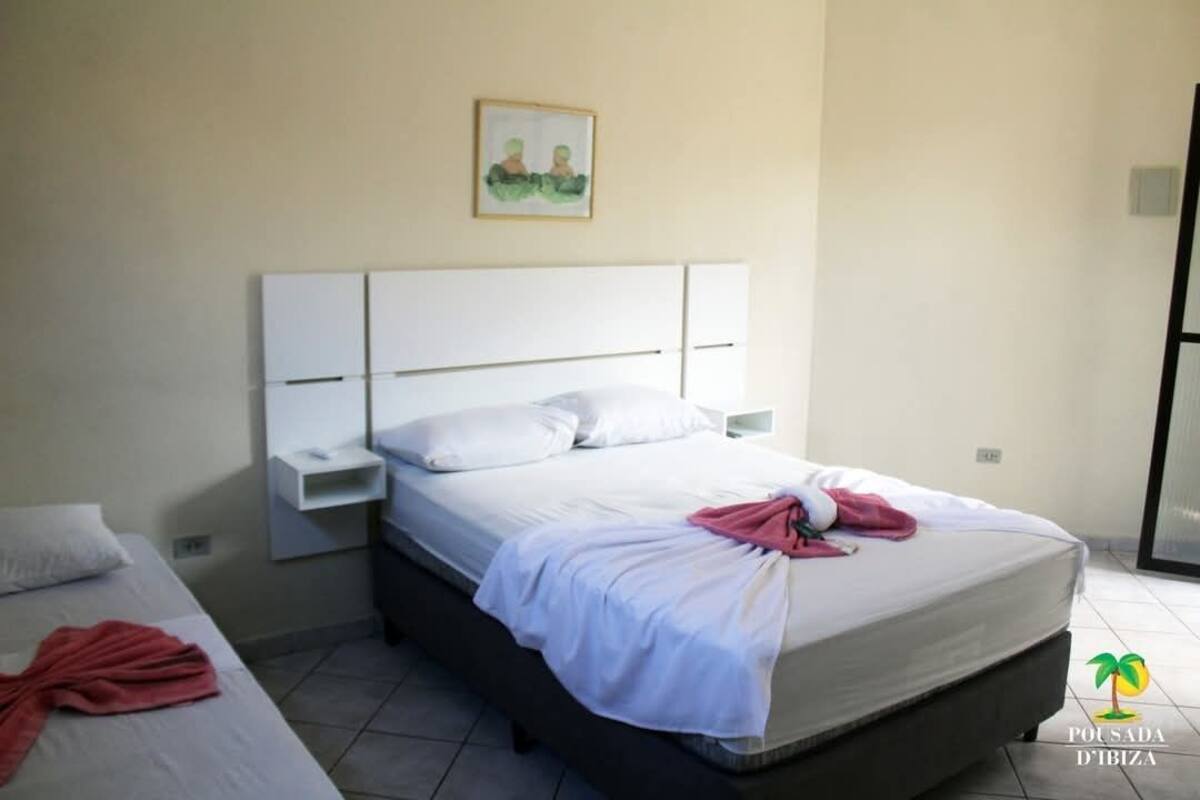 A hotel room with a bed, a nightstand, and a wall-mounted shelf.