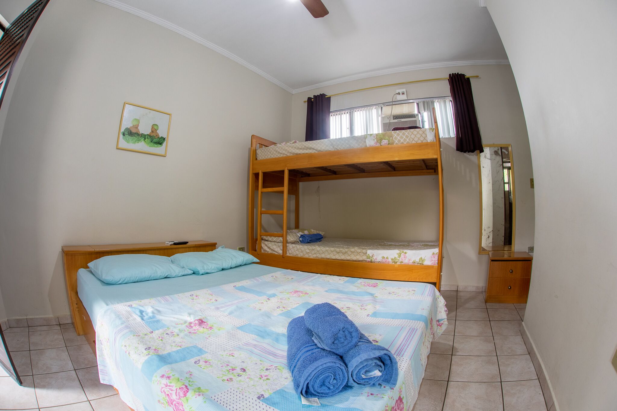 A bedroom with a bunk bed, a single bed, a bedside table, a mirror, and a window with curtains.