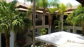 A courtyard with a white table, palm trees, and a building with a tiled roof. - Pousada D'Ibiza (Itanhaém)