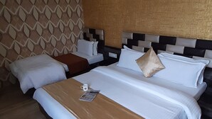 A double bed with a brown headboard and white bedding, a nightstand with a lamp, and a patterned wall. - Hotel Shahi Darbar (Navsari)