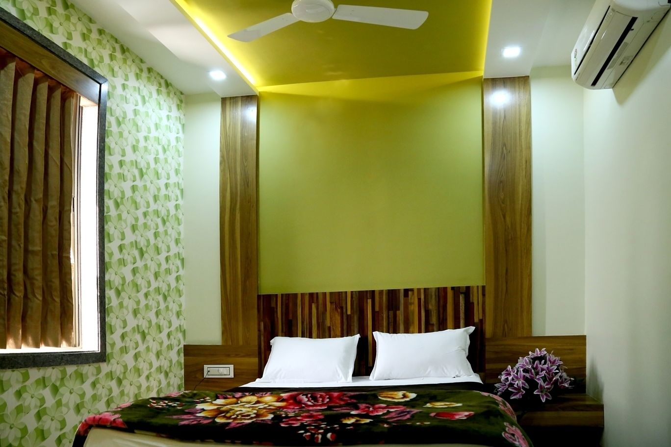 A bedroom with a bed, a ceiling fan, an air conditioner, and a window with curtains.