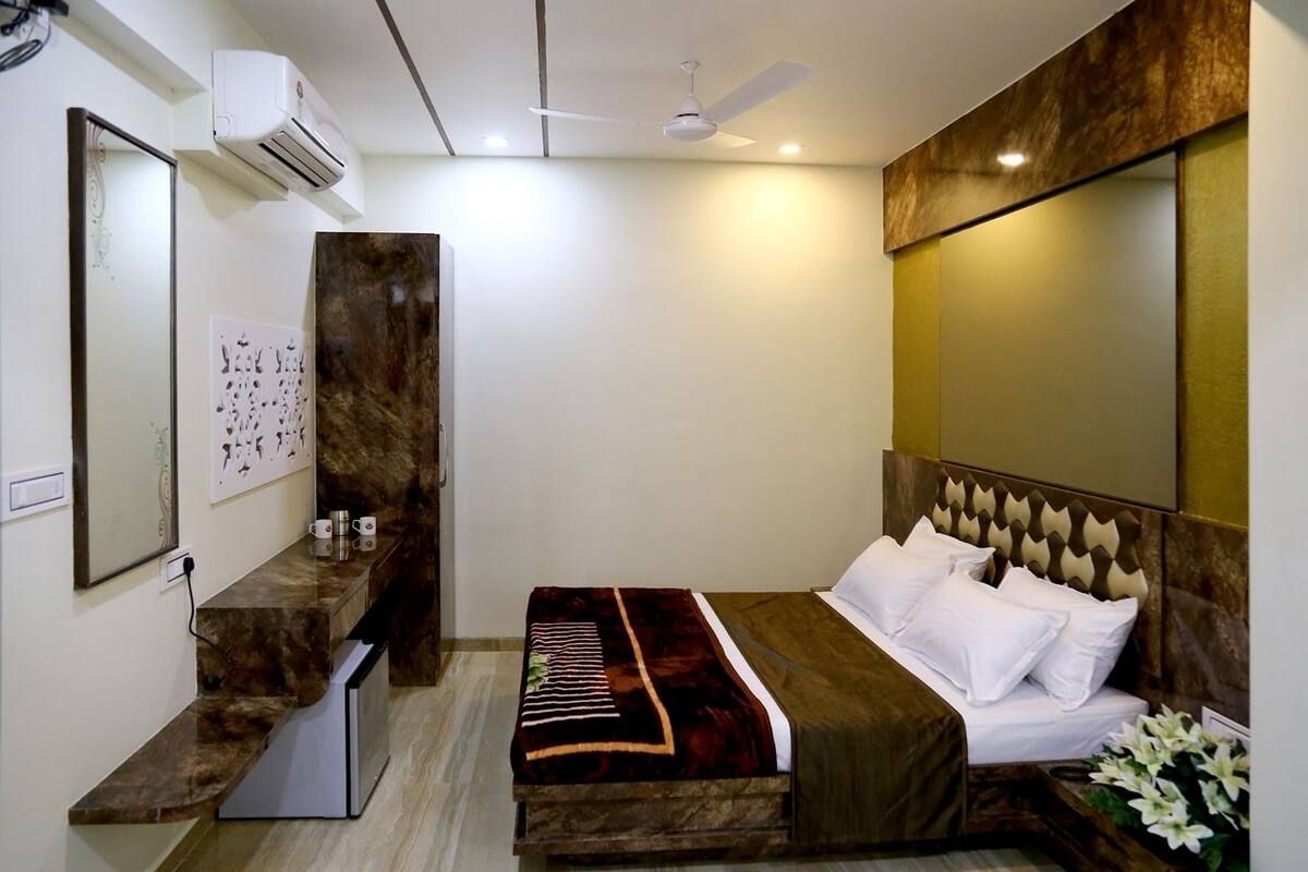 A bedroom with a bed, bedside table, mirror, and wall-mounted air conditioning unit.