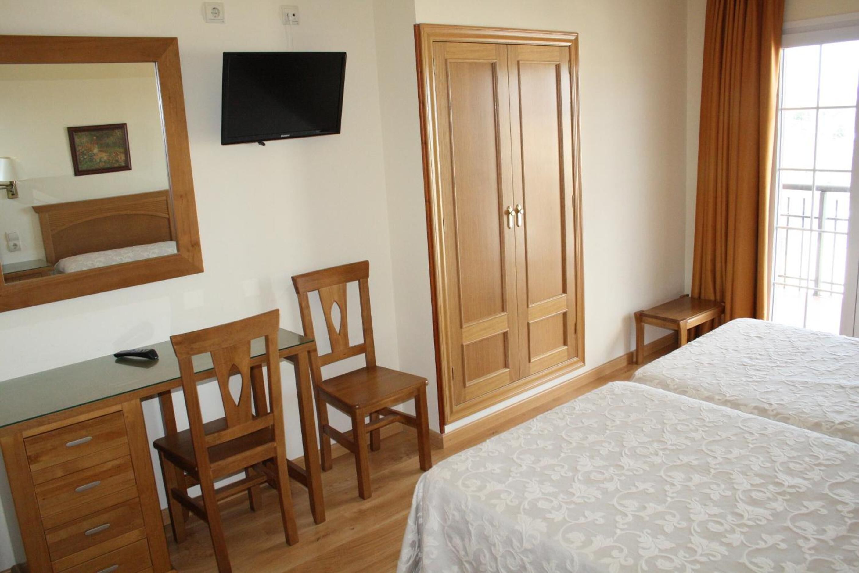 Un dormitorio con un armario de madera, un escritorio con silla, una cama y un televisor en la pared.