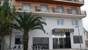 Een hotel met balkon, een palmboom en terraszitplaatsen.