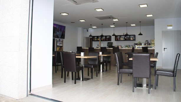 Een modern restaurant met een bar, verschillende tafels en stoelen, en een keuken op de achtergrond.