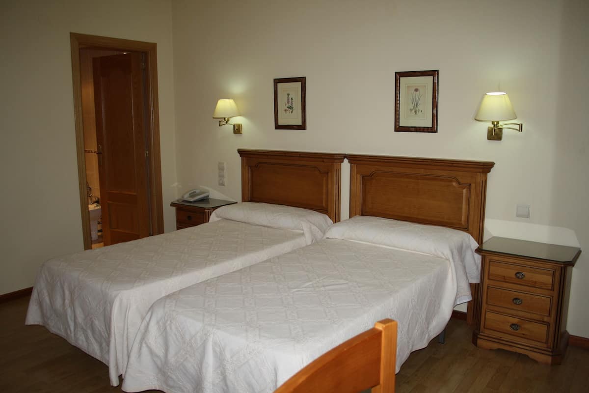 Een kamer met twee enkele bedden, een houten nachtkastje met een lamp en een klein dressoir.