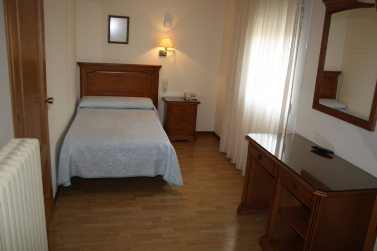 Een slaapkamer met een houten bed, een nachtkastje met een lamp, een kaptafel en een radiator.