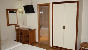 Een slaapkamer met twee bedden, een houten bureau, een stoel, een televisie en een badkamer met douche en bad.