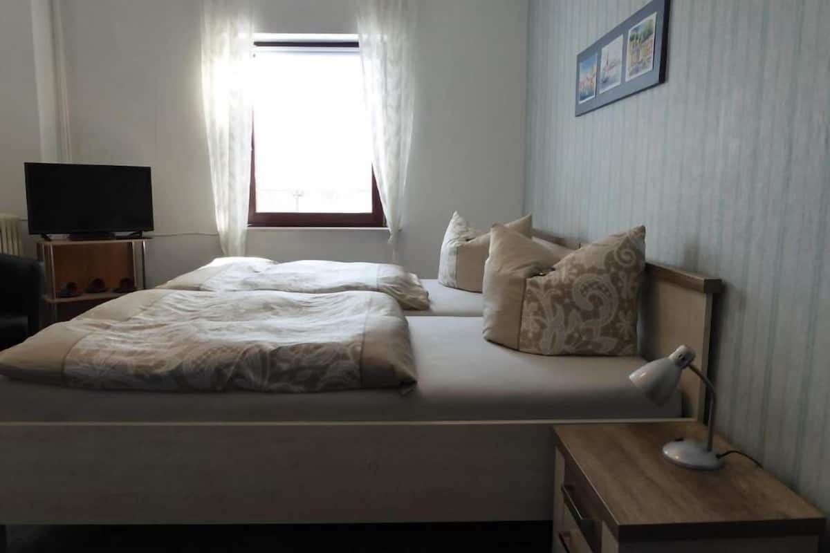 Un dormitorio con dos camas, televisor, escritorio con lámpara y ventana con cortinas.